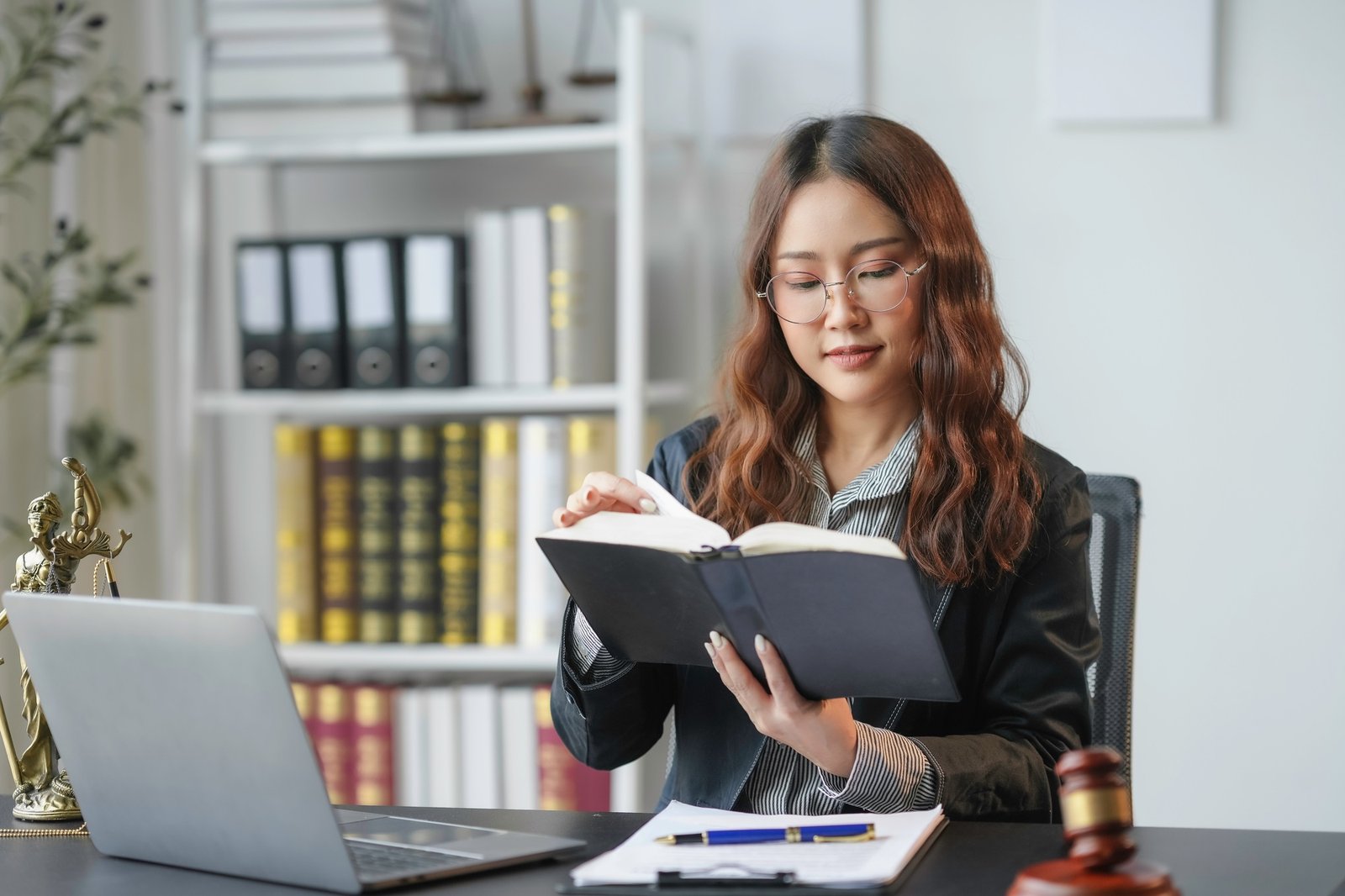 Lawyer is sitting at her desk reading a law book, preparing for an upcoming case